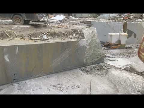 Video: the diamond wire saw makes the base cut. The beaded wire is threaded through both horizontal bores and around the flywheel, then drawn slowly through the granite as the saw retracts along its tracks, a little like a cheese cutter. The base cut always comes first, so the block cannot settle onto the wire.