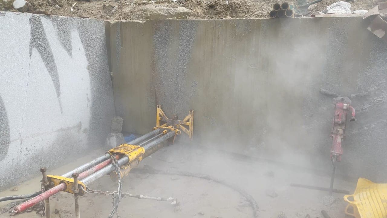 The drill rig boring into the granite face at De Lank, dust rising as the 75mm bit works through the stone