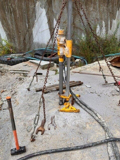 The pneumatic drill rig anchored on top of the bench, set up to bore the 75mm vertical hole down through the granite