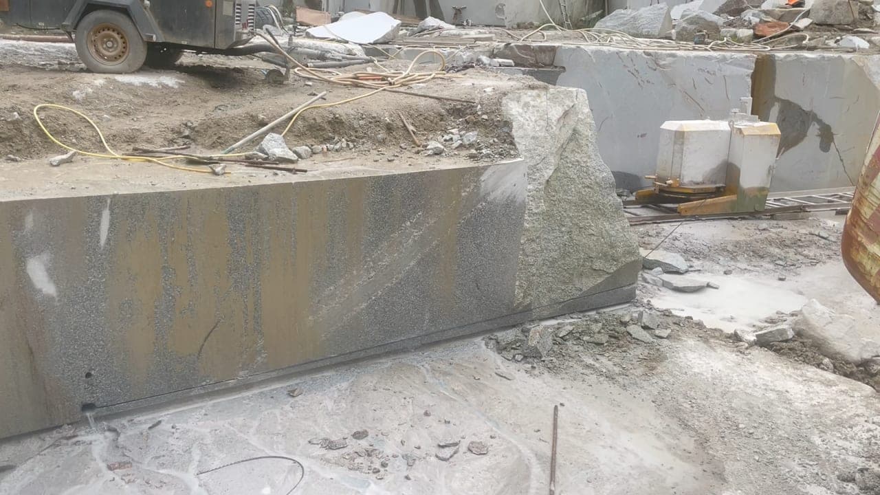 The drill rig boring into the granite face at De Lank, dust rising as the 75mm bit works through the stone